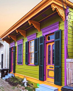 Brightly painted purple, green, and gold house with black shutters and decorative front porch