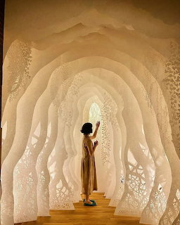Woman standing inside a large white paper-cut art installation with layered arches and floral patterns