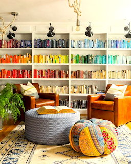 Living room with rainbow-organized bookshelf, orange chairs, and colorful boho cushions