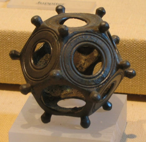Bronze spherical ornament with circular openings and knobs on beige fabric