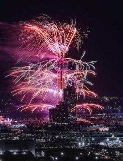 Fireworks bursting around Reunion Tower in Dallas at night with city skyline in the background