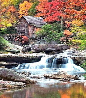 Rustic wooden mill with water wheel next to flowing waterfall in autumn forest with colorful red and orange trees