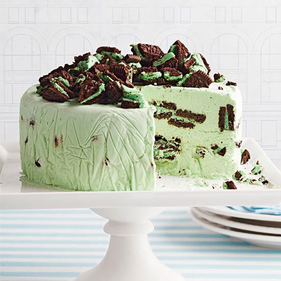 Mint green layered cake with chocolate cookie pieces on top, displayed on white pedestal stand