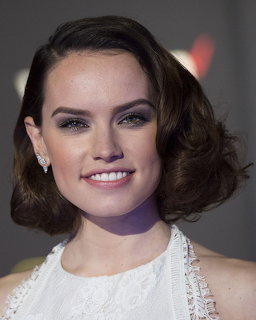 Close-up portrait of Daisy Ridley smiling in a white sleeveless dress