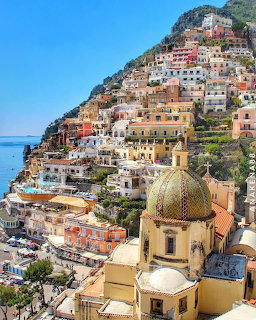 Colorful buildings on a steep hillside in Positano Italy with a golden church dome and sea view