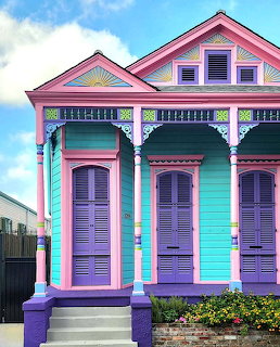 Colorful Victorian house with purple shutters and pink trim in pastel turquoise, blue sky background
