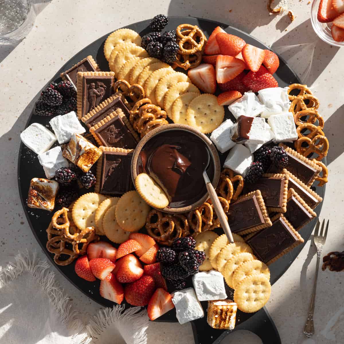 Dessert board with chocolate, strawberries, cookies, pretzels, and marshmallows arranged in a circle