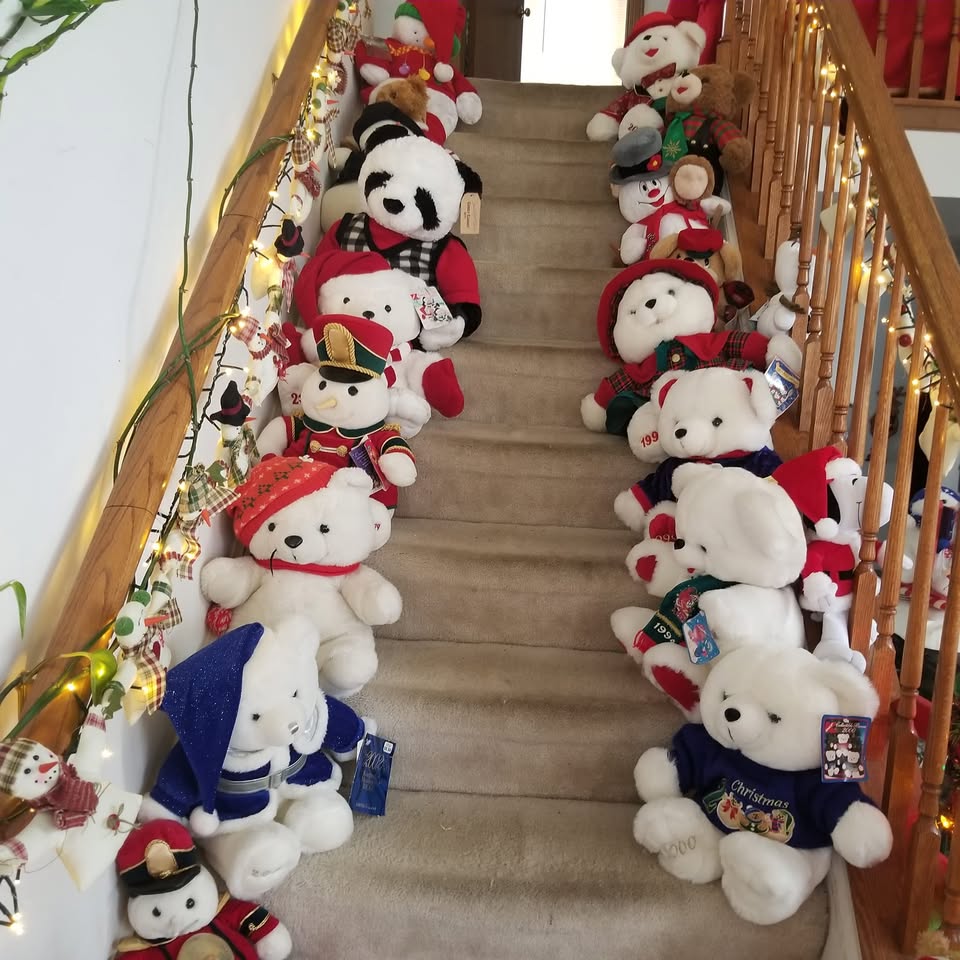 Many plush snowman toys lined up on stairs with garland and Christmas lights on the railing