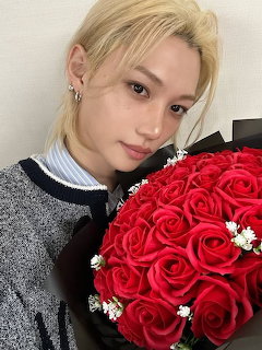 Young man with blonde hair holding red rose bouquet, wearing grey knit sweater