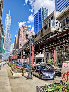 Downtown street with parked cars, tall buildings, and an elevated train overhead