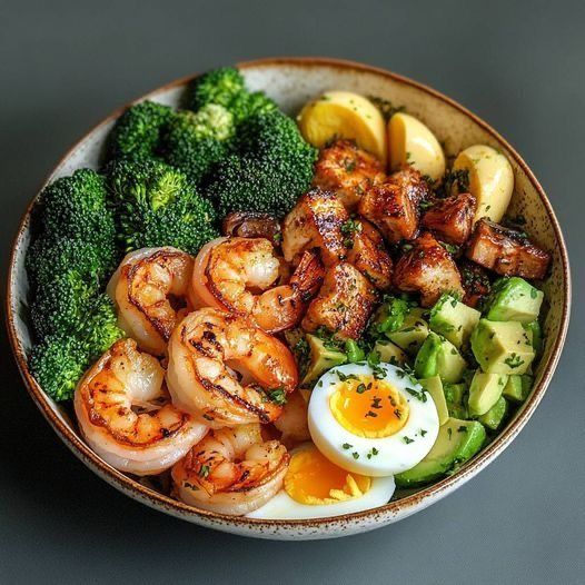 Bowl with grilled shrimp, broccoli, avocado, soft-boiled egg, and potatoes on gray background