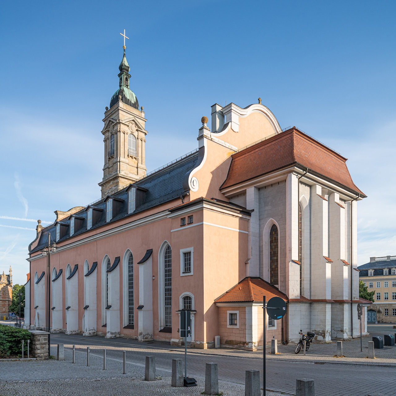 White and peach baroque church building with red tile roof and tall bell tower under blue sky