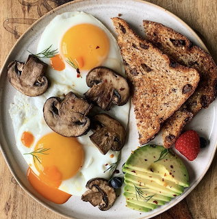 Breakfast plate with fried eggs, mushrooms, toast, avocado and strawberry from above