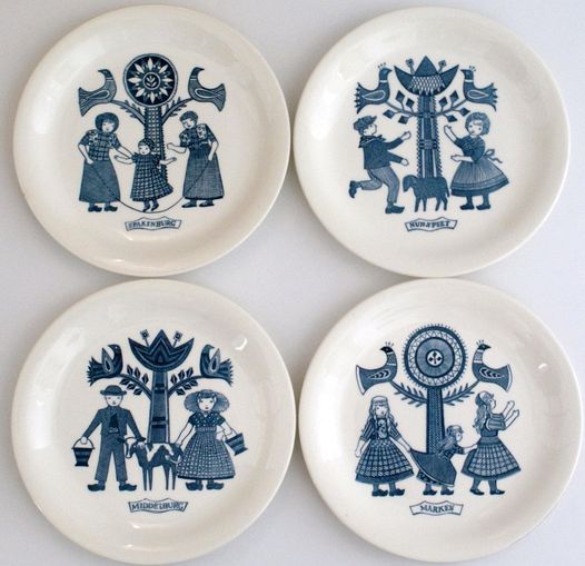 Four white plates with blue folk-style illustrations arranged in a 2x2 grid