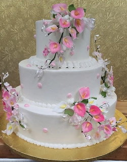Three-tier white wedding cake adorned with pink and white sugar calla lilies and green leaves