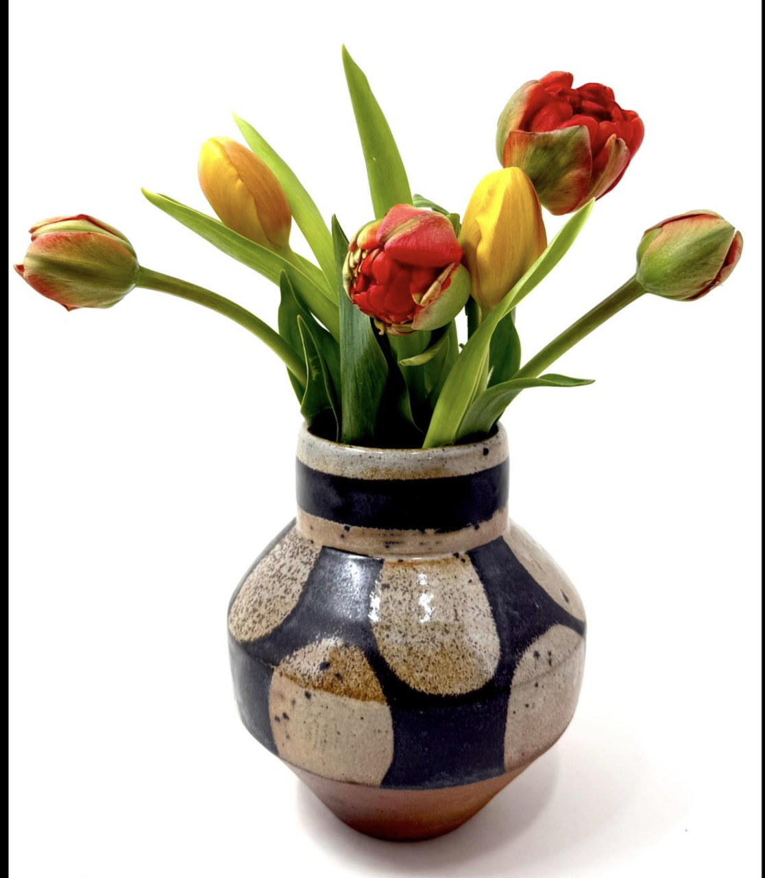 Red and yellow tulips in a round ceramic vase with dark blue and beige pattern on white background