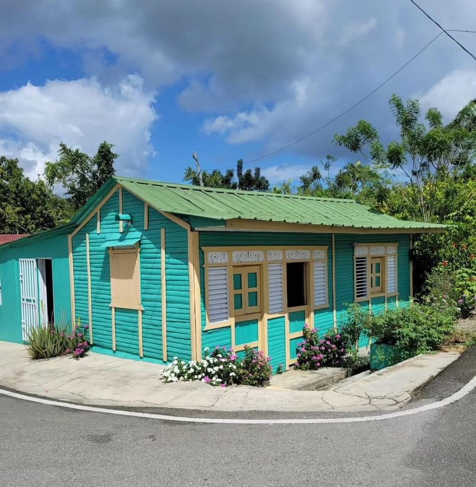 Turquoise wooden house with green roof and yellow doors on a curved street corner
