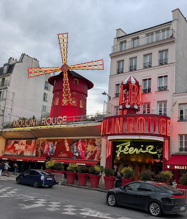 Exterior of the Moulin Rouge in Paris with the red windmill, bright signs, and cars on the street