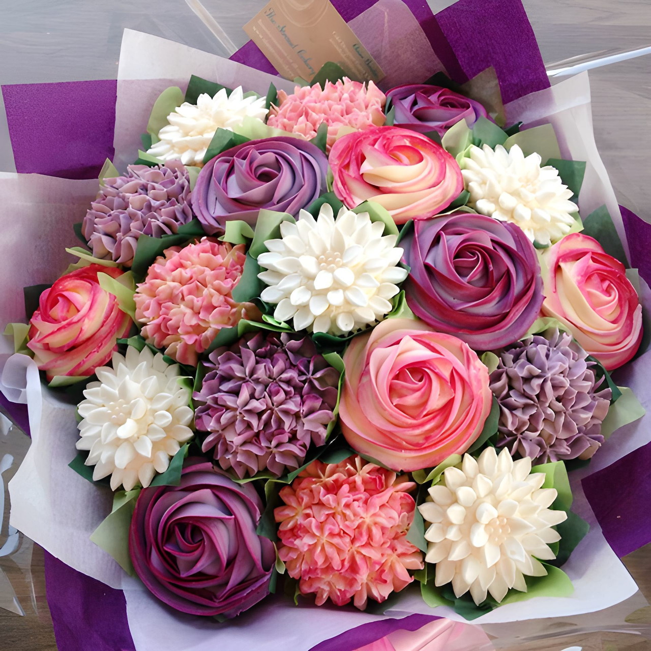 Cupcake bouquet with buttercream flowers in pink, purple and white, wrapped in purple paper