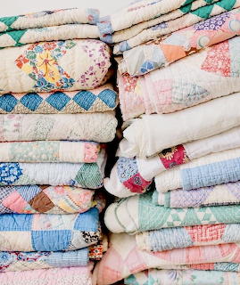 Stack of folded vintage patchwork quilts in pastel colors
