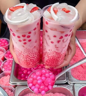 Two pink bubble tea cups with whipped cream and strawberries on tray with pink heart decorations