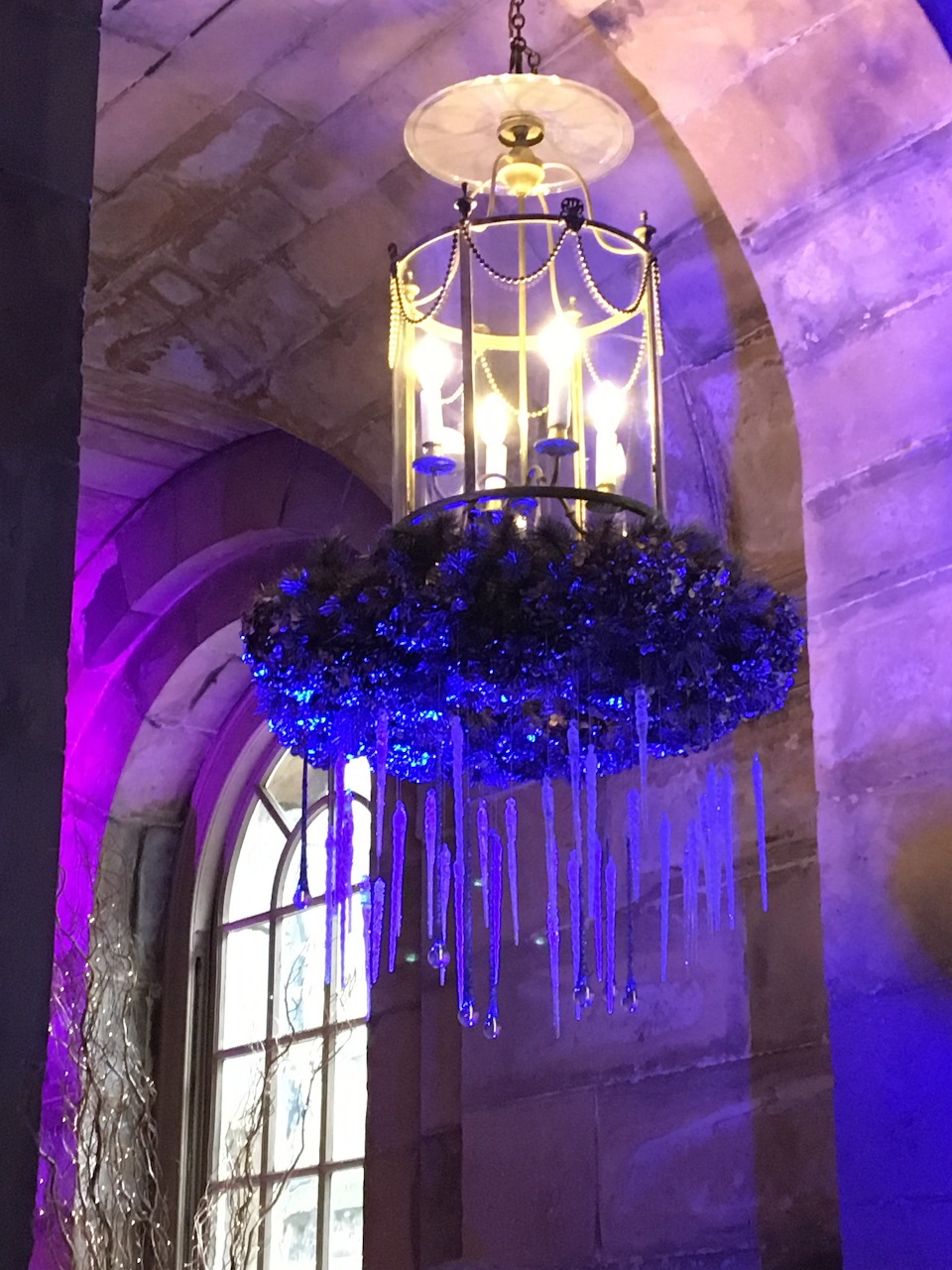 Ornate chandelier with purple crystals hanging in stone archway with violet lighting