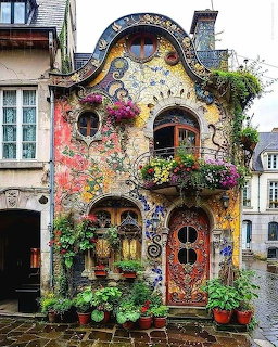 Colorful mosaic house facade with curved windows, flower boxes, and potted plants