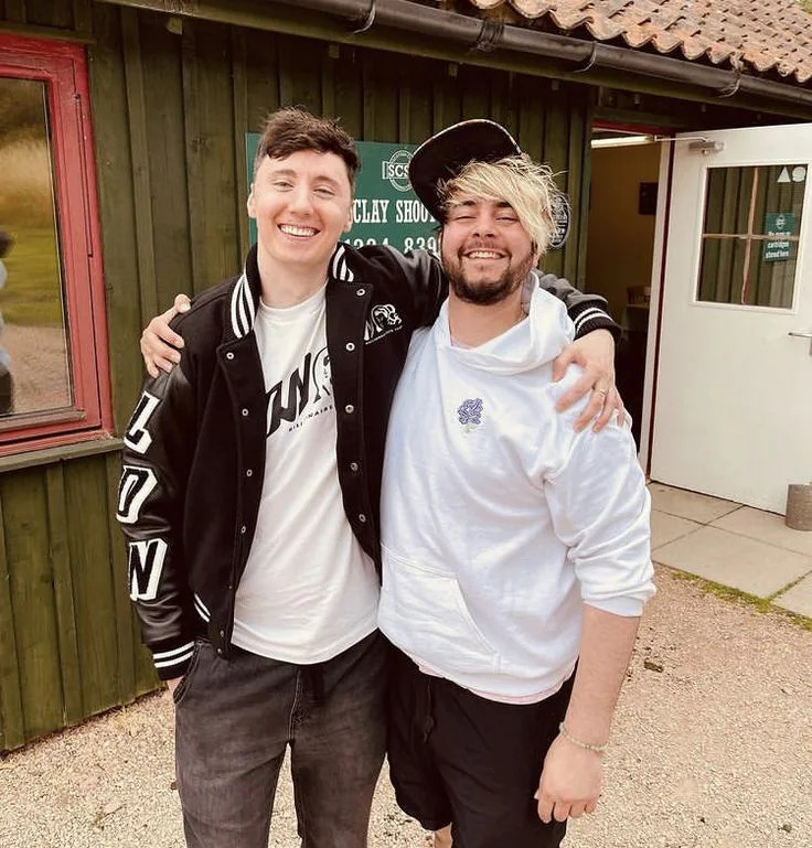 Two smiling men posing arm in arm outdoors by a rustic building