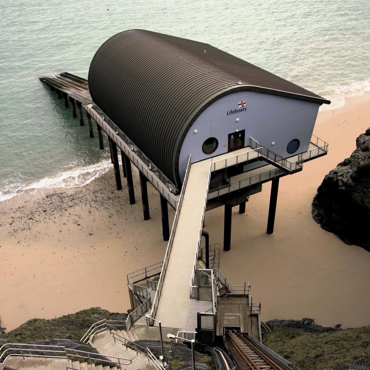 Lifeboat house on stilts over a sandy beach with a long walkway and calm sea
