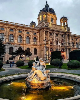Kunsthistorisches Museum Vienna at dusk with illuminated fountain and sculptures in foreground