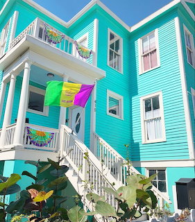 Turquoise beach house with white stairs, balcony, and colorful flags