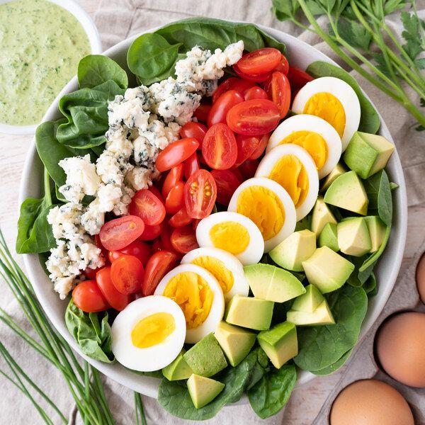 Spinach salad bowl with cherry tomatoes, boiled eggs, avocado, and crumbled cheese