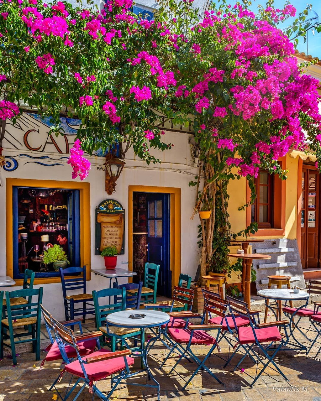 Outdoor cafe with pink bougainvillea flowers, colorful metal chairs and tables in sunny courtyard