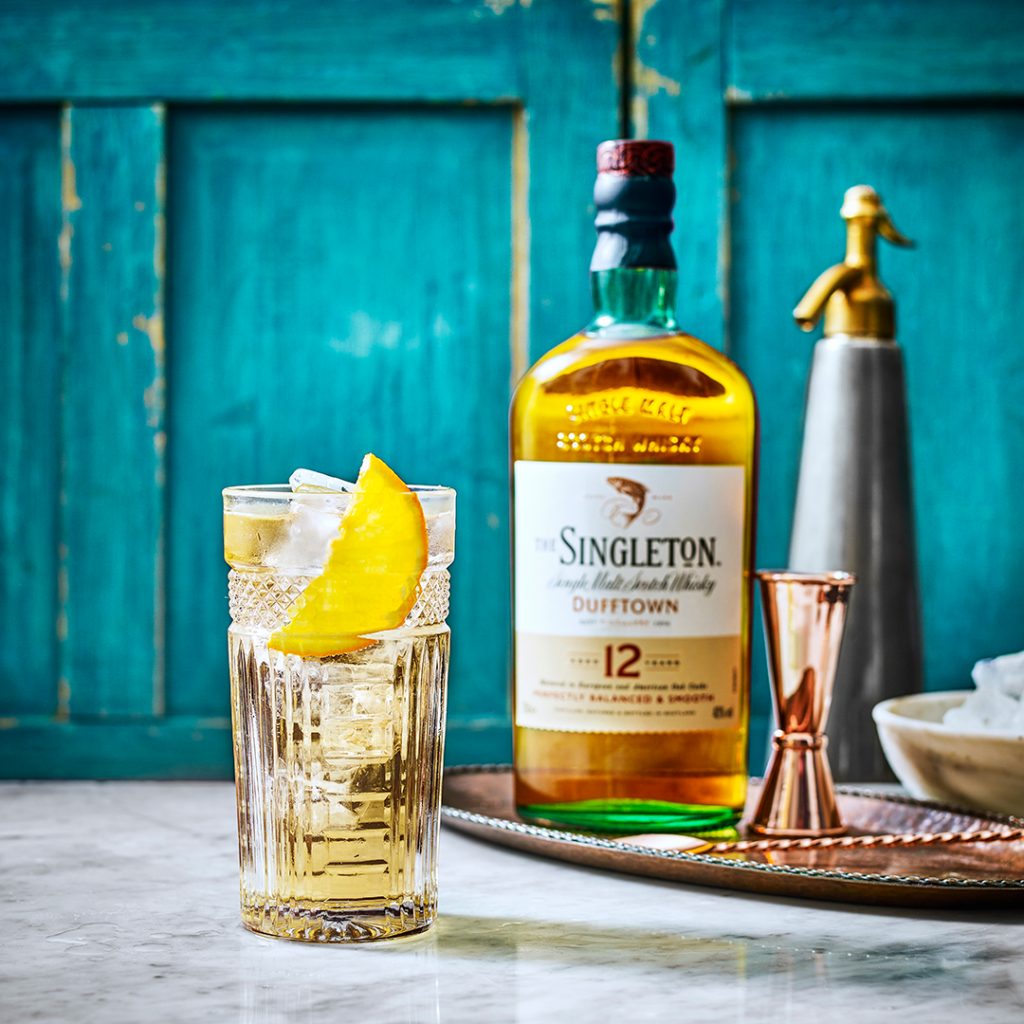 Glass of whisky cocktail with lemon peel beside a bottle of Singleton 12 on a tray
