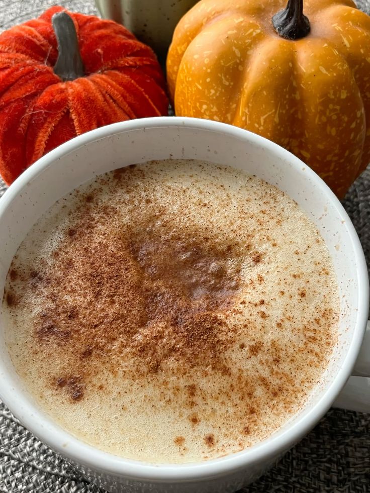 Pumpkin spice latte with cinnamon topping next to orange and yellow pumpkins