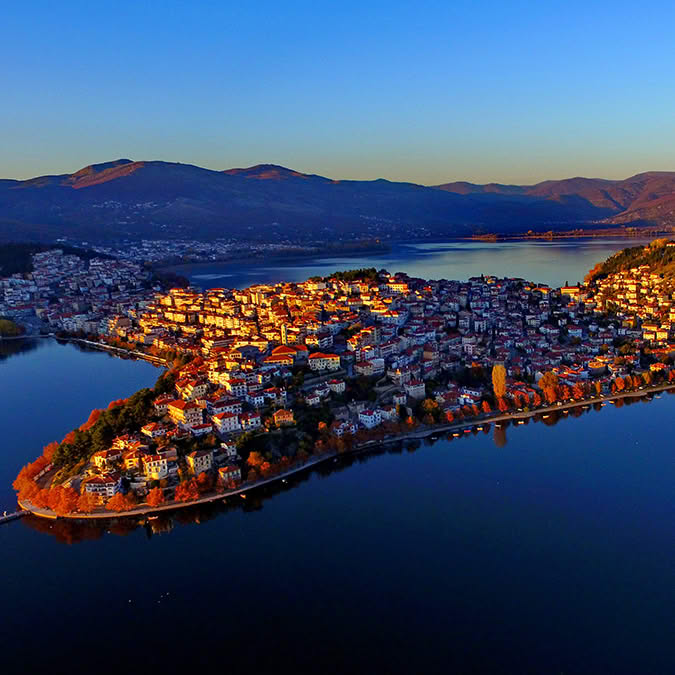 Aerial view of Kastoria city on a peninsula by a lake with mountains in the background at dusk