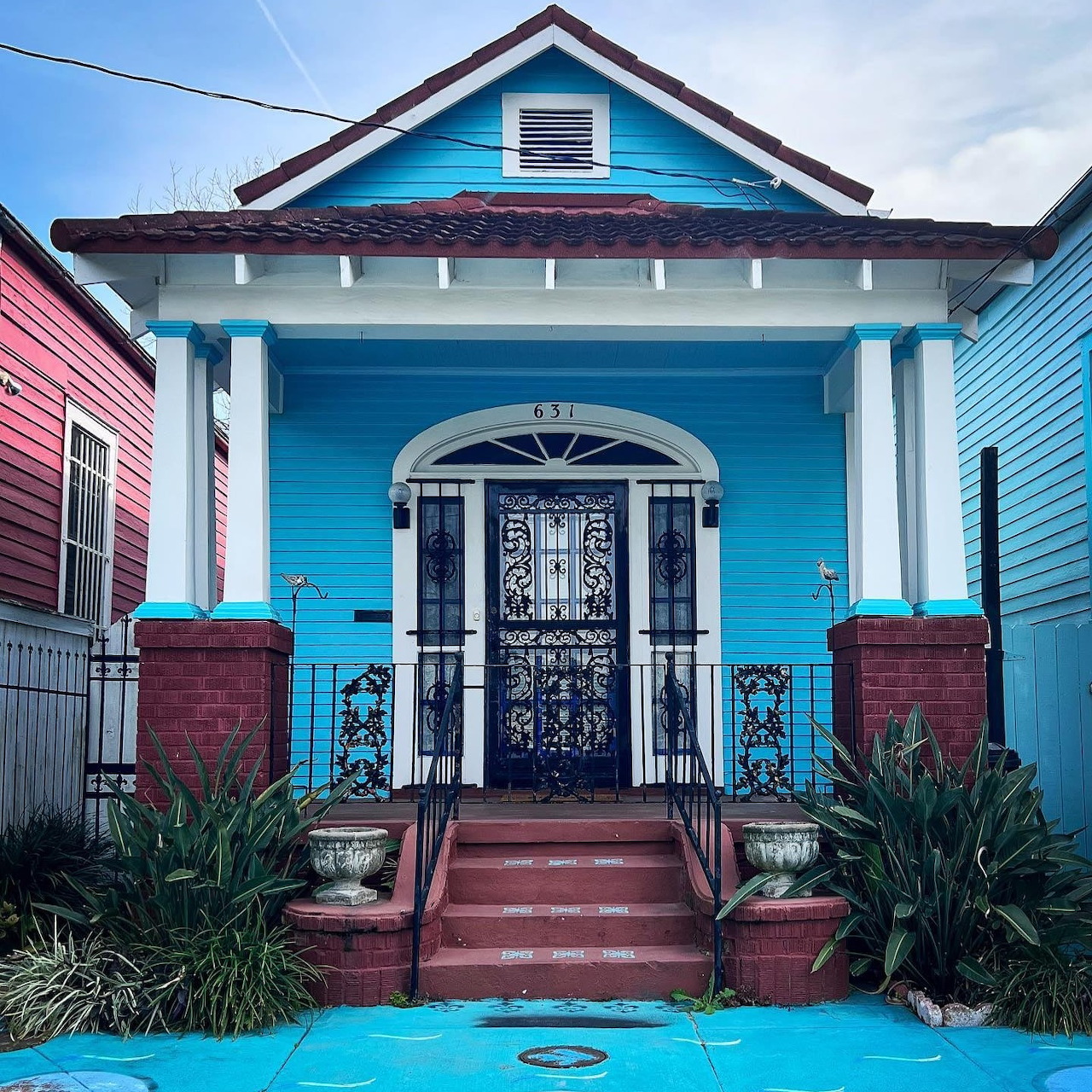 Bright blue house with white porch columns, brick steps, and decorative iron front door