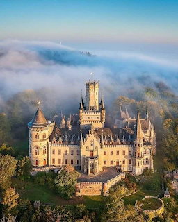 White castle with towers rising above foggy forest on hilltop at dawn