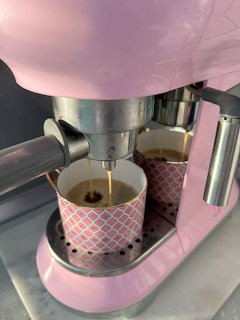 Pink espresso machine pouring fresh coffee into a small patterned cup on a marble surface