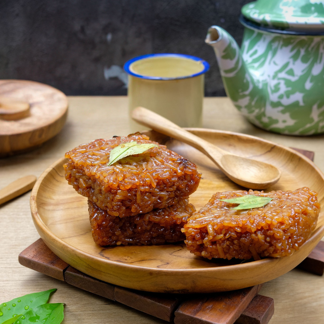 Wajik ketan sticky rice cakes on a wooden plate with a wooden spoon, teapot, and cup in the background