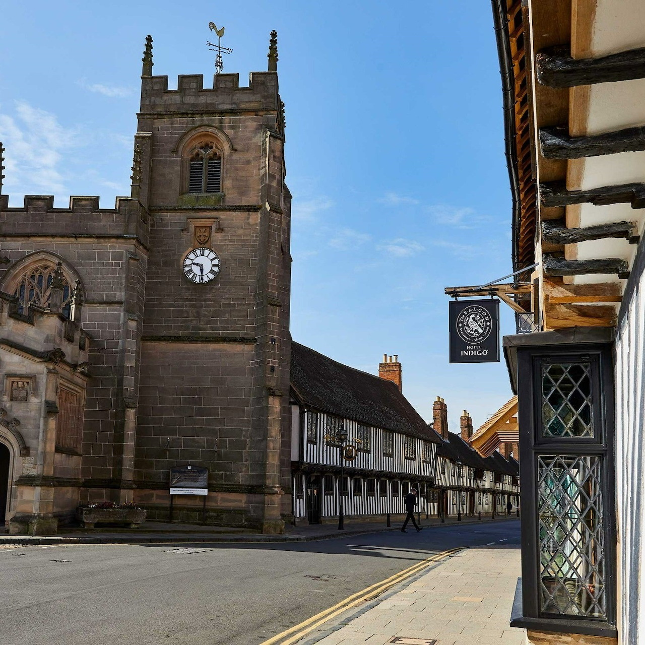 Stone church tower with clock on historic English street with Tudor buildings
