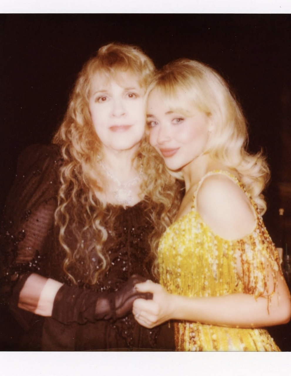 Two blonde women in sparkly evening gowns posing together, one in gold sequins, one in brown