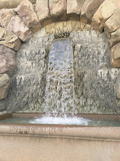 Water cascading down a stone wall through a rustic rock arch into a basin below