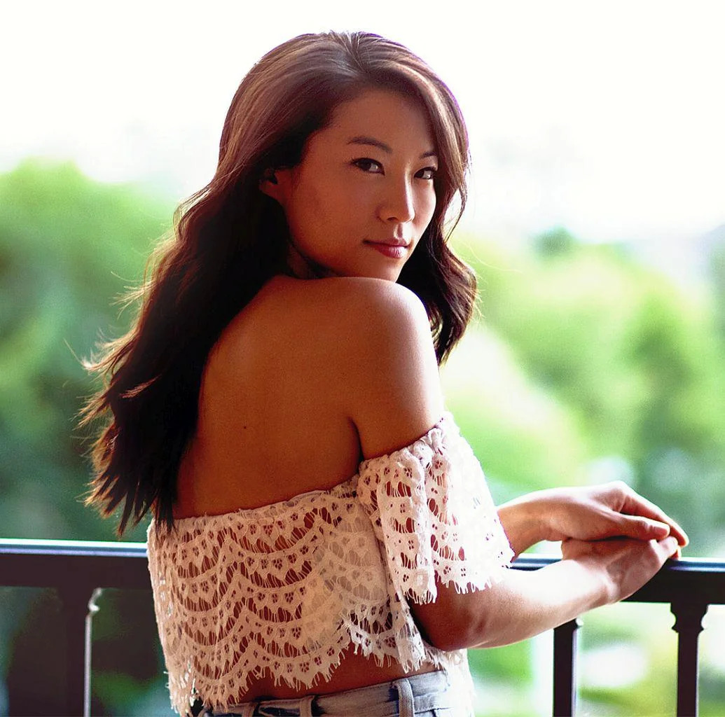 Woman in off-shoulder lace top looking over shoulder on balcony with greenery in background