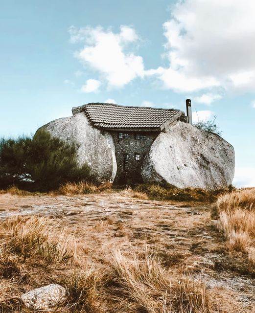 Stone house built between massive boulders on a rocky hillside in Portugal, dry grass in foreground