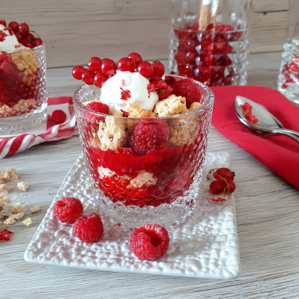 Layered fruit crumble dessert in glass with berries, cream, and crumble topping on white plate