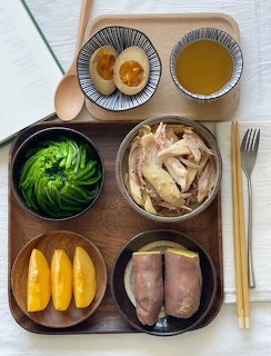 Wooden tray with bowls of shredded chicken, avocado rose, boiled eggs, mango slices, sweet potato, and broth