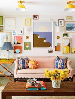 Eclectic living room with pink couch, colorful wall art, wooden coffee table, yellow flowers, and modern decor