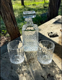 Crystal decanter with square stopper and two cut crystal glasses on a rustic wooden table outdoors