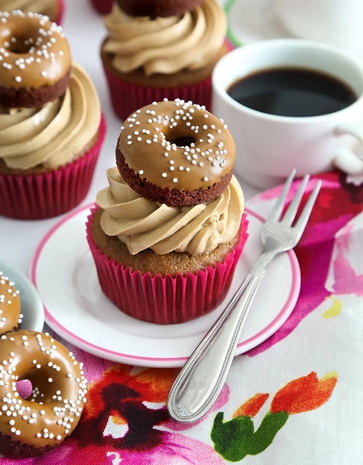 Coffee cupcakes with mini chocolate donuts on top, frosted with coffee buttercream, served alongside a cup of black coffee
